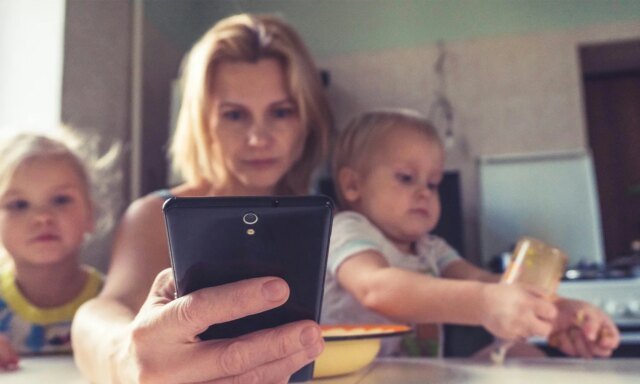 A-woman-uses-smartphone-while-sitting-with-children.jpg