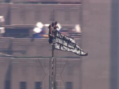 Duas pessoas sobem ao topo do Empire State Constructing de Nova York e exibem um banner